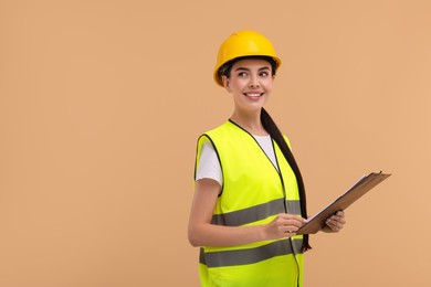 Photo of Engineer in hard hat holding clipboard on beige background, space for text