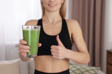 Photo of Young woman in sportswear with glass of fresh smoothie at home, closeup