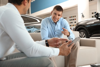 Photo of Young salesman working with client in modern car dealership