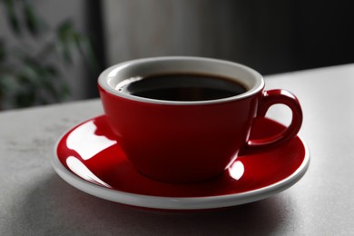 Red cup with aromatic coffee on wooden table indoors, closeup