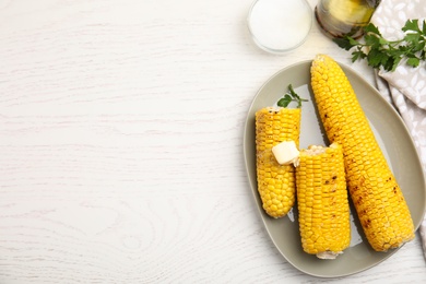Photo of Fresh grilled corn cobs with butter on white wooden table, flat lay. Space for text