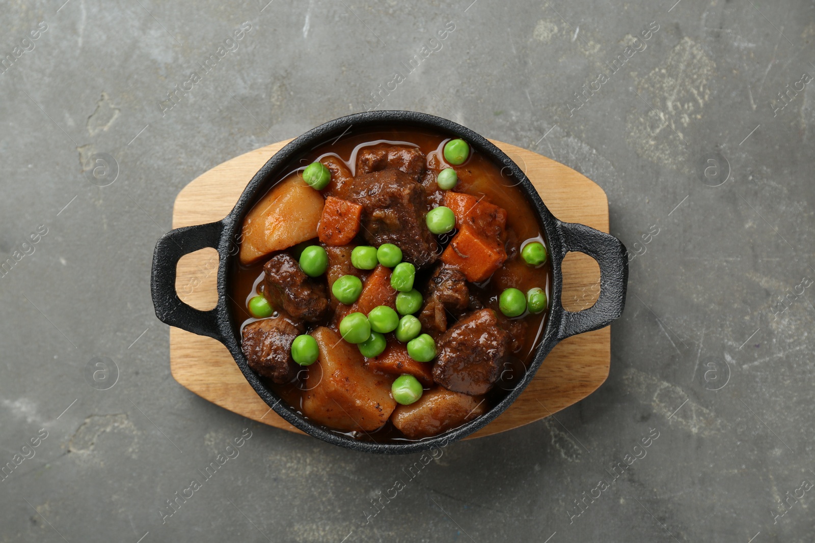 Photo of Delicious beef stew with carrots, peas and potatoes on grey table, top view