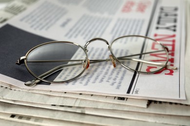 Glasses on stack of newspapers, closeup view