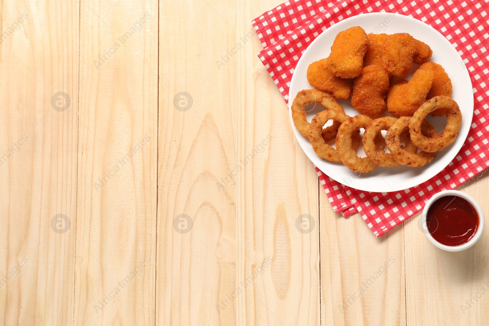 Photo of Tasty fried onion rings, chicken nuggets and ketchup on wooden table, flat lay. Space for text