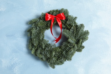 Photo of Christmas wreath made of fir tree branches with red ribbon on light blue textured background