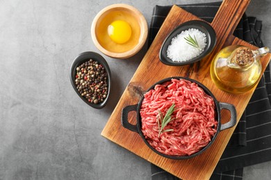 Photo of Raw ground meat in bowl, spices, egg and oil on grey table, flat lay. Space for text