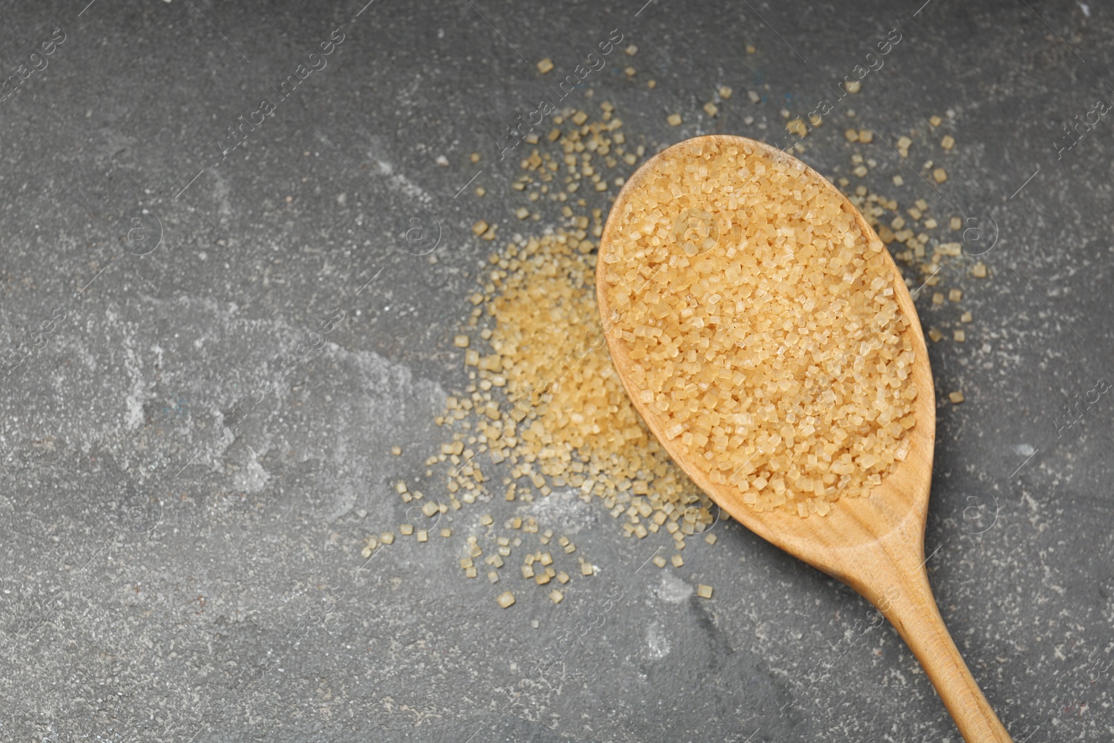 Photo of Spoon with brown sugar on grey textured table, top view. Space for text