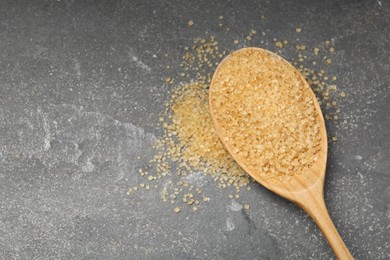 Spoon with brown sugar on grey textured table, top view. Space for text