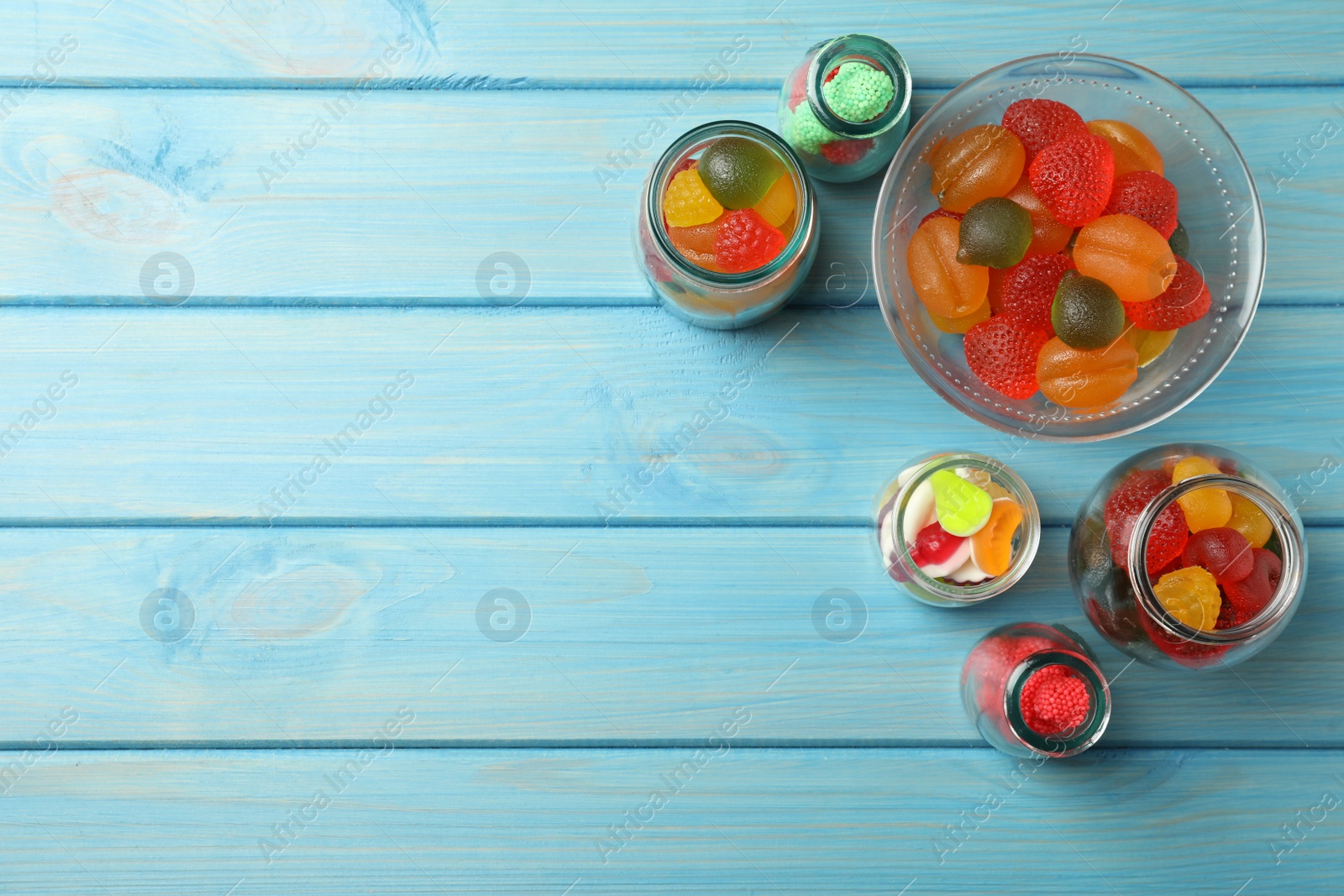 Photo of Delicious gummy candies on light blue wooden background, flat lay. Space for text