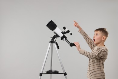 Surprised little boy with telescope pointing at something on light grey background, space for text