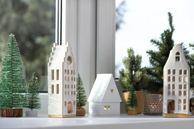 Beautiful house shaped candle holders and small fir trees on windowsill indoors