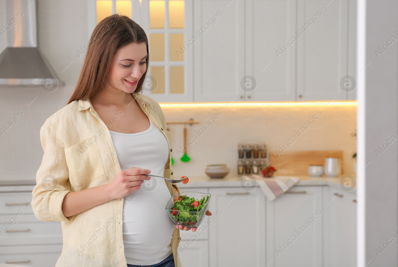 Photo of Young pregnant woman with vegetable salad in kitchen, space for text. Healthy eating