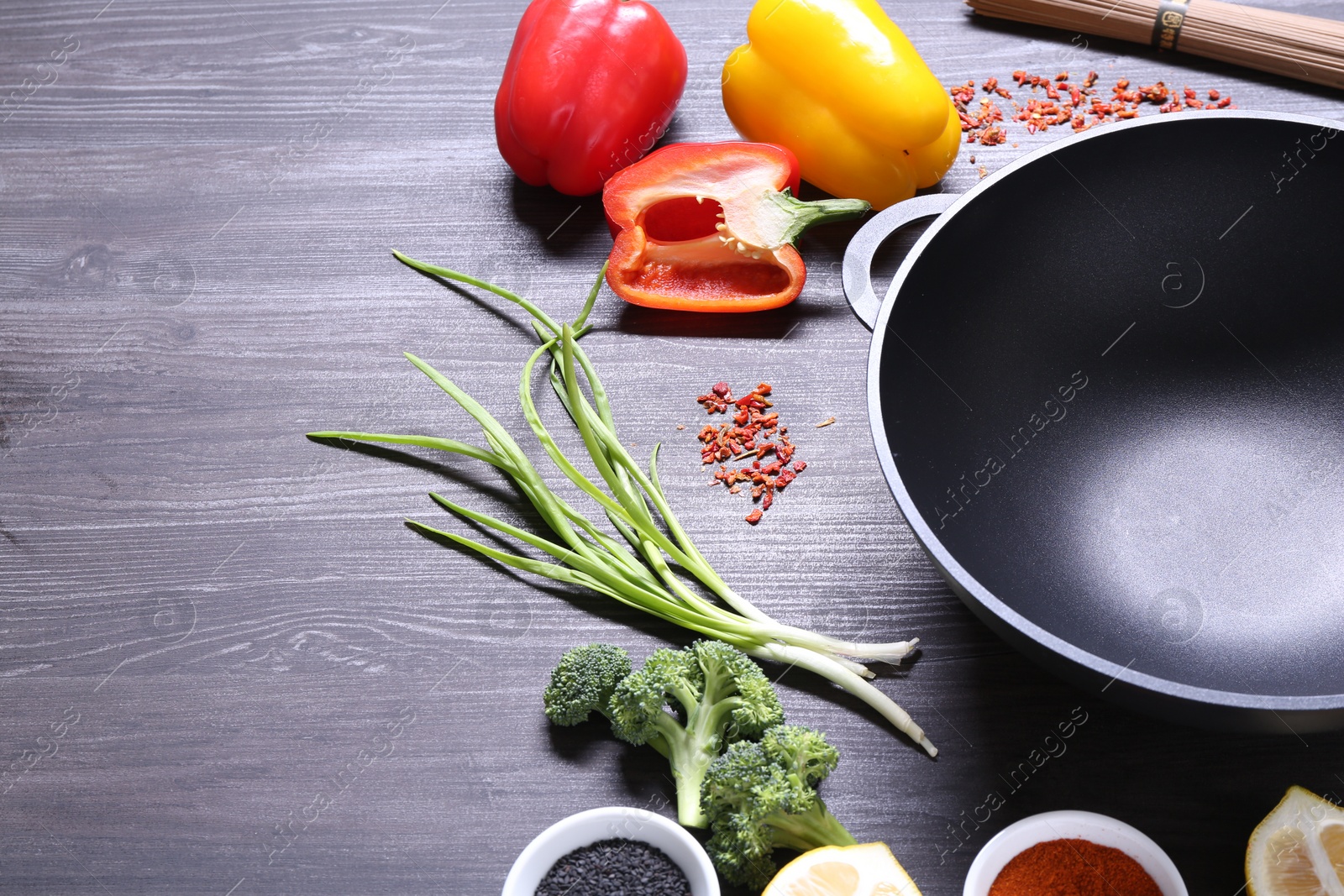 Photo of Empty iron wok and ingredients on dark grey wooden table. Space for text