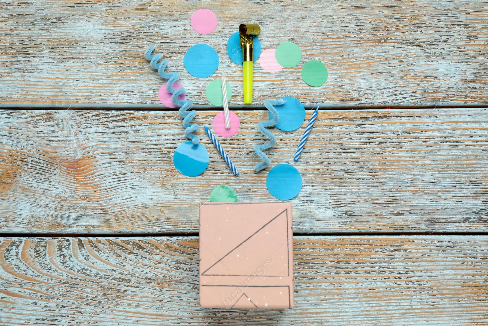 Photo of Pink box with colorful party items on wooden table, flat lay