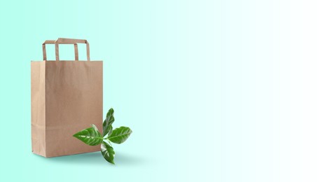 Paper shopping bag and green leaves on color background, space for text. Eco friendly lifestyle