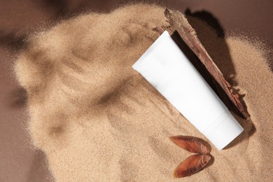 Photo of Tube of body cream, seashell and tree bark on sand against brown background. Space for text