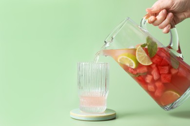 Photo of Woman pouring tasty watermelon drink with lime from jug into glass on pale light green background, closeup