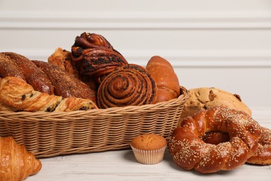 Photo of Wicker basket with different tasty freshly baked pastries on white wooden table