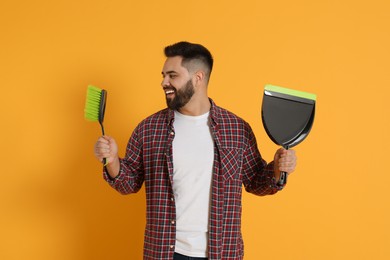 Young man with broom and dustpan on orange background