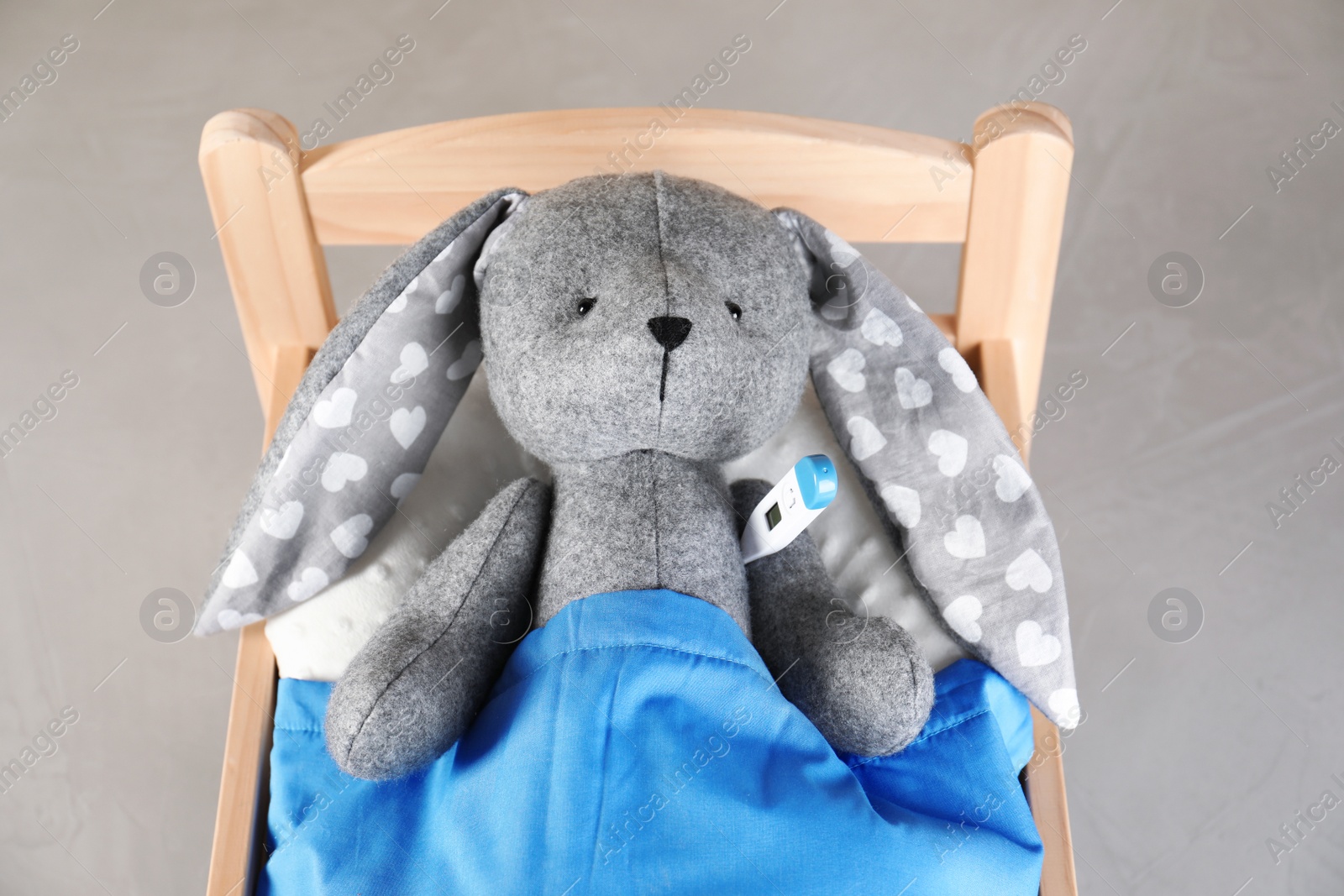 Photo of Toy bunny with thermometer lying in bed on grey background, above view. Children's hospital