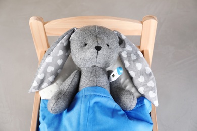 Photo of Toy bunny with thermometer lying in bed on grey background, above view. Children's hospital