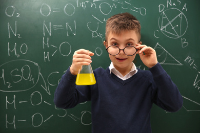 Photo of Schoolboy holding flask near chalkboard with chemical formulas