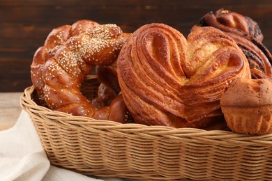 Wicker basket with different tasty freshly baked pastries on table, closeup