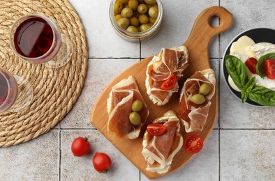 Tasty sandwiches with cured ham, tomatoes and olives on tiled table, flat lay