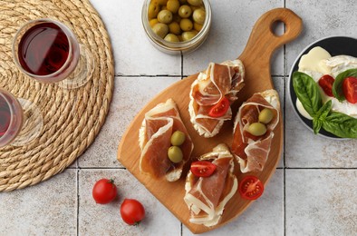 Photo of Tasty sandwiches with cured ham, tomatoes and olives on tiled table, flat lay