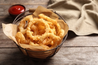 Photo of Homemade crunchy fried onion rings in wire basket on wooden background, closeup