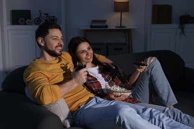 Photo of Happy couple with popcorn watching TV at home in evening