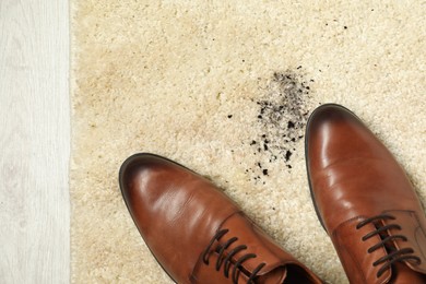 Photo of Brown shoes and mud on beige carpet, top view. Space for text