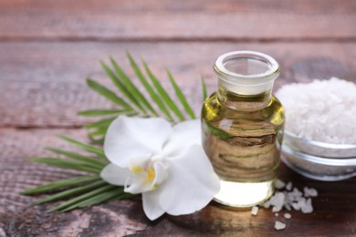 Bottle of essential oil, sea salt and orchid flower on wooden table, closeup. Space for text