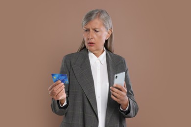 Photo of Worried businesswoman with credit card and smartphone on brown background. Be careful - fraud