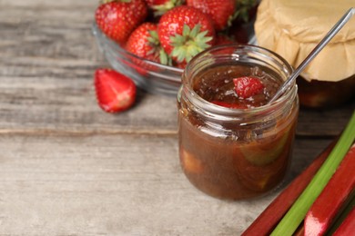 Photo of Tasty rhubarb jam, stems and strawberries on wooden table. Space for text