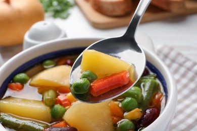 Photo of Spoon with delicious turnip soup above bowl, closeup