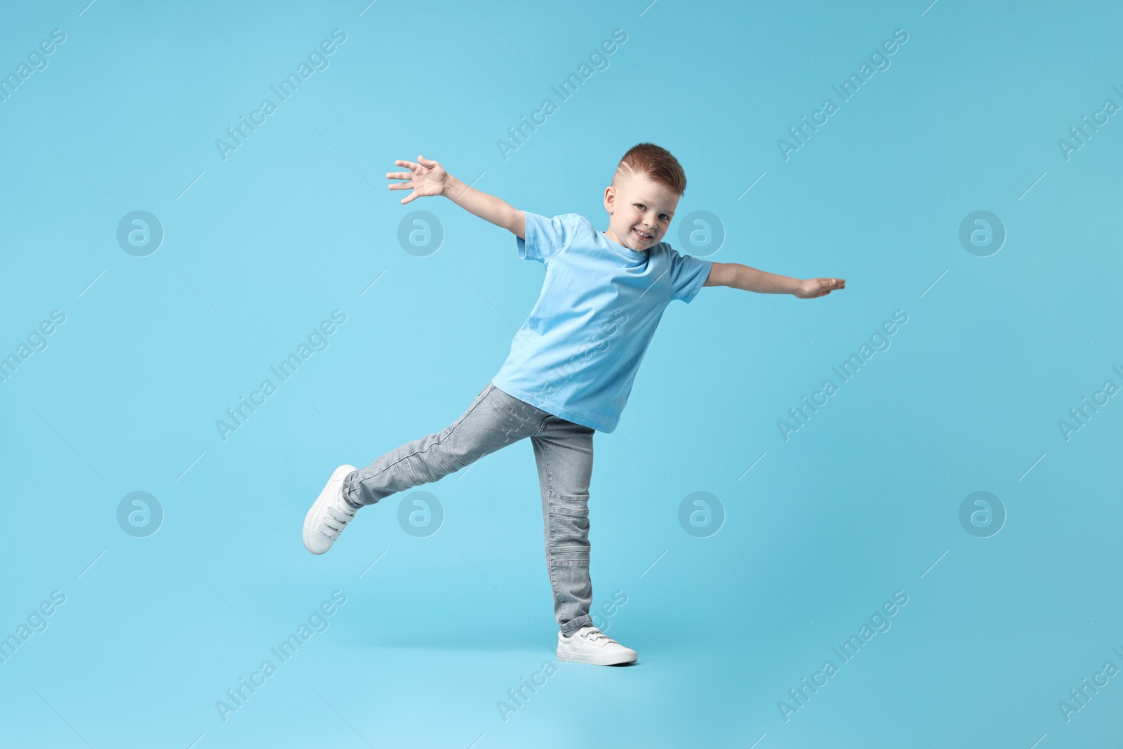 Photo of Happy little boy dancing on light blue background