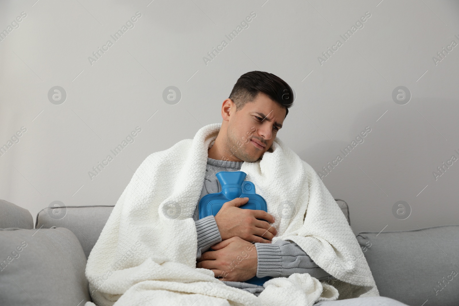 Photo of Ill man with hot water bottle suffering from cold at home