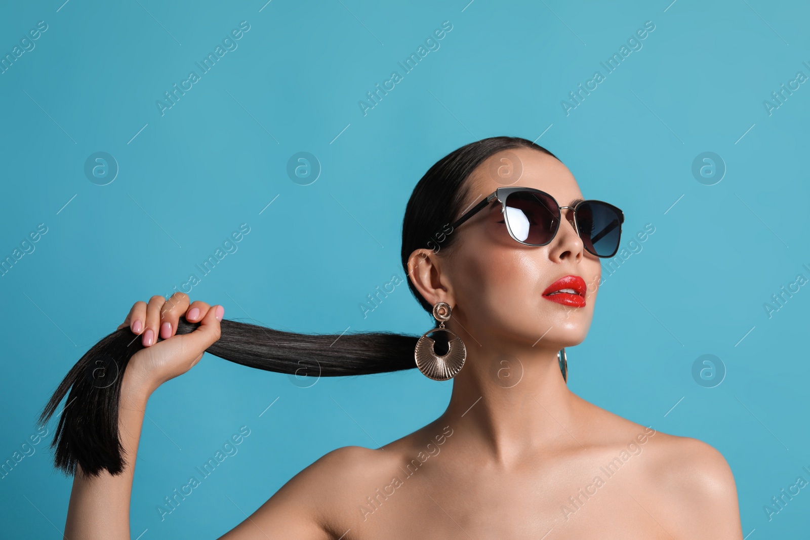 Photo of Attractive woman in fashionable sunglasses touching her hair against light blue background