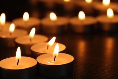 Photo of Burning tealight candles on dark surface, closeup