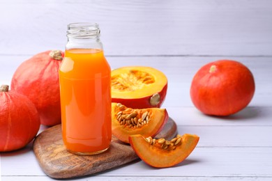Photo of Tasty pumpkin juice in glass bottle and pumpkins on white wooden table. Space for text