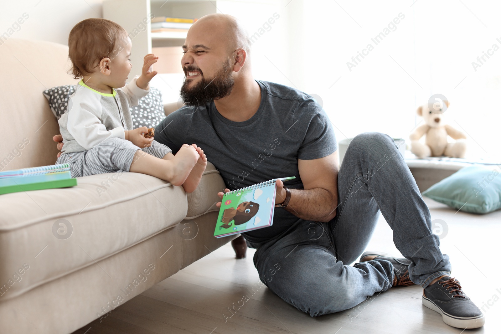 Photo of Dad reading book with his little son in living room