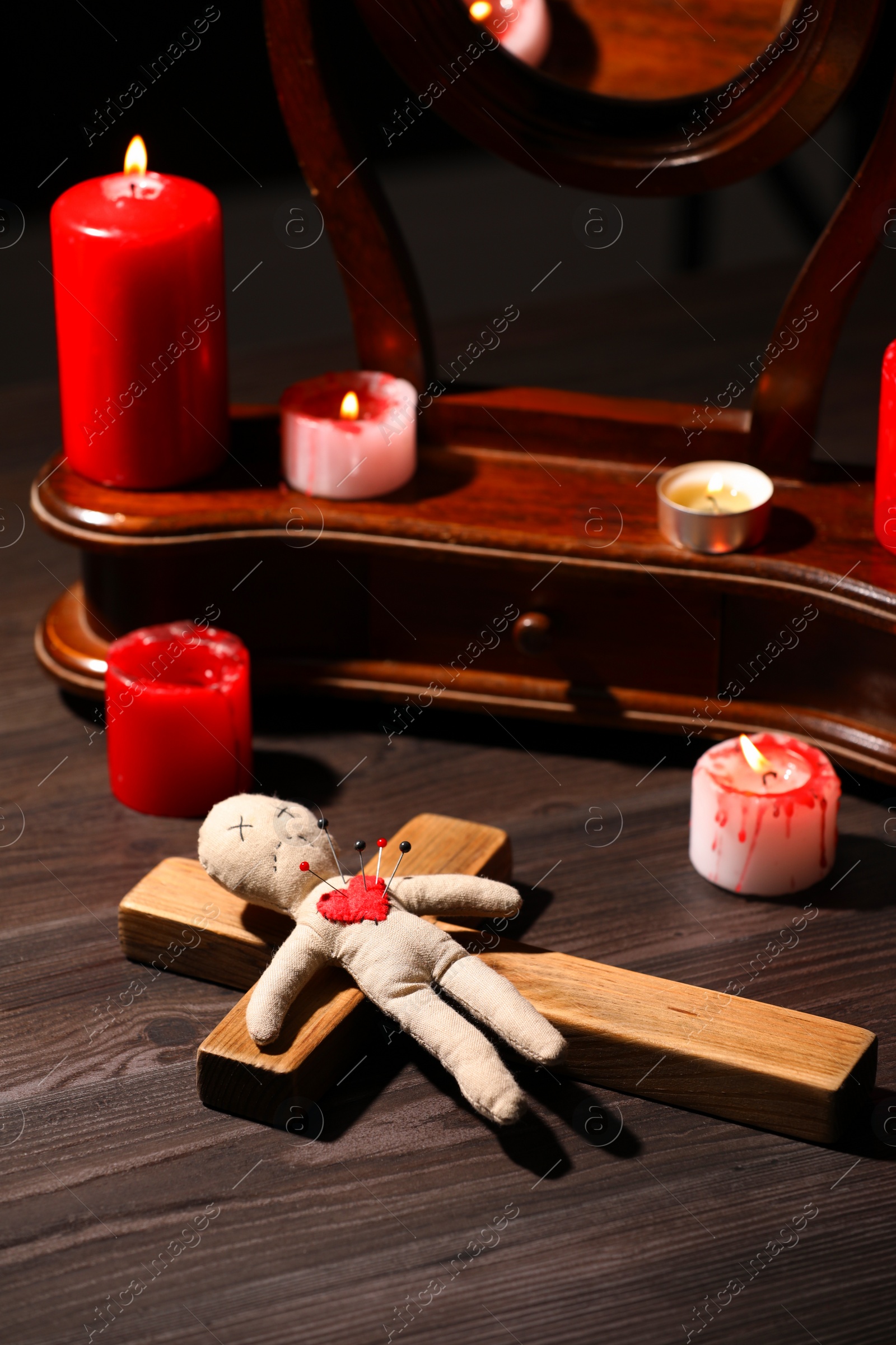 Photo of Voodoo doll with pins in heart and ceremonial items on wooden table