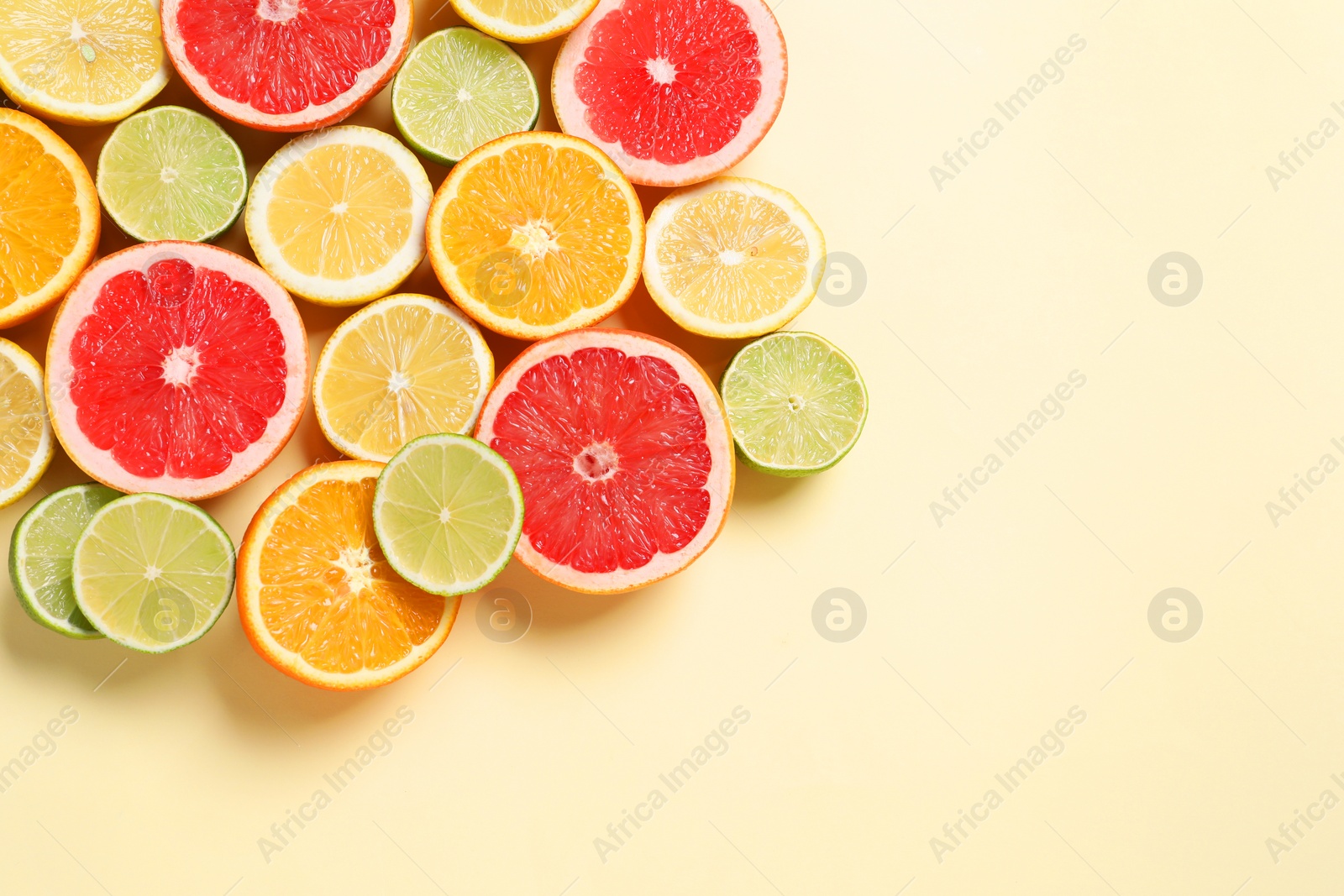 Photo of Different cut citrus fruits on beige table, flat lay. Space for text