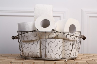 Photo of Soft toilet paper rolls in metal basket on wicker table, closeup