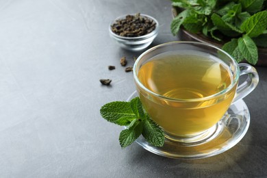 Photo of Cup of hot aromatic mint tea on grey table. Space for text