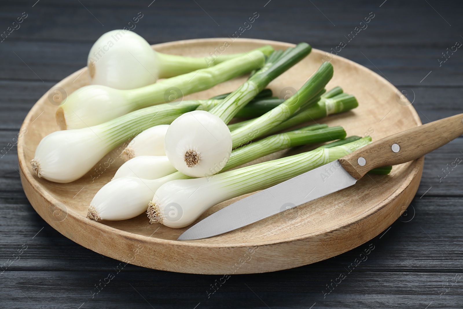 Photo of Tray with green spring onions and knife on black wooden table, closeup