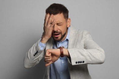 Emotional man checking time on grey background. Being late concept