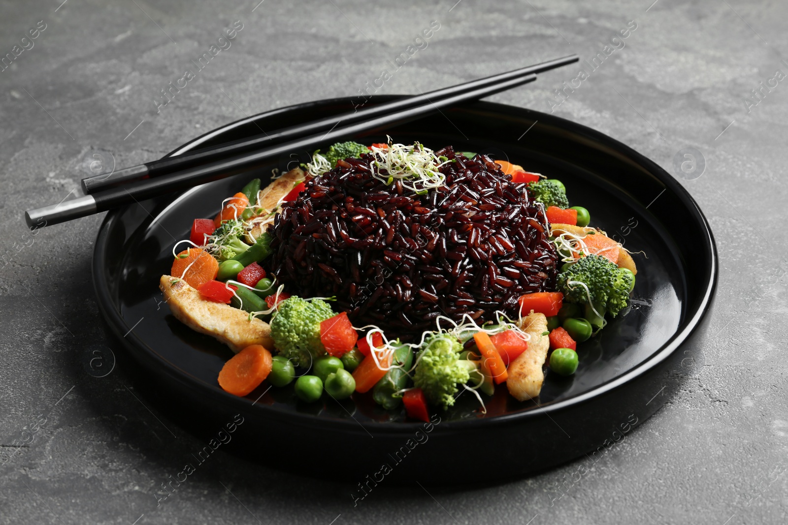 Photo of Plate of cooked brown rice with vegetables and chopsticks on table