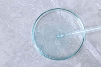 Photo of Glass pipette and petri dish with liquid on grey marble table, top view. Space for text